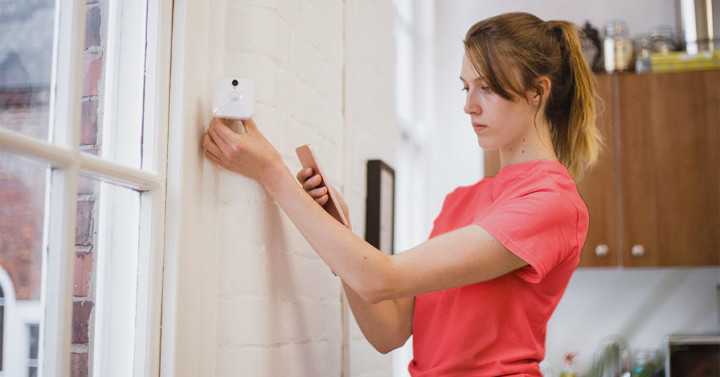 A woman holding a phone adjusting a security camera
