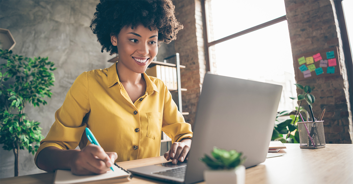 Woman writing on a notepad and looking at a computer