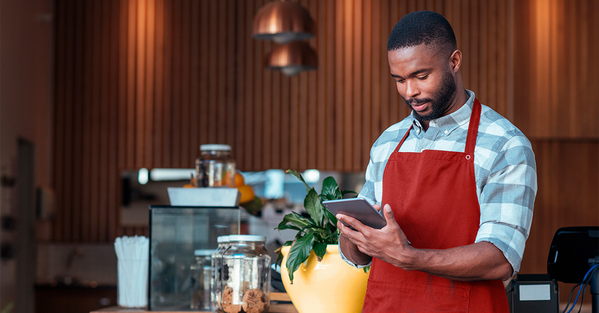 Man in a cafe wearing an apron looking at a tablet