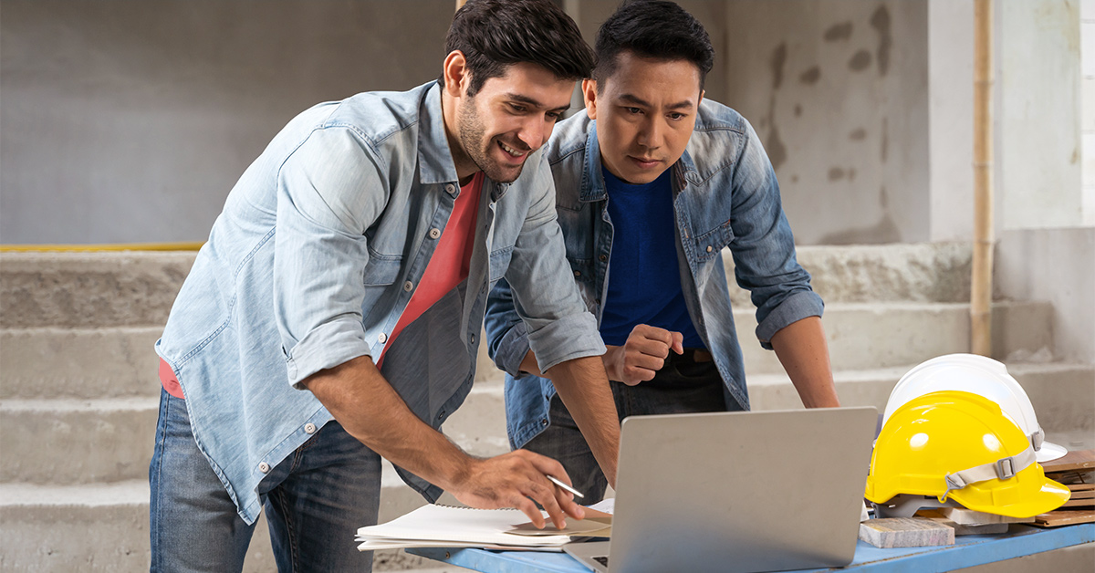 Two men at a construction site talking next to a computer