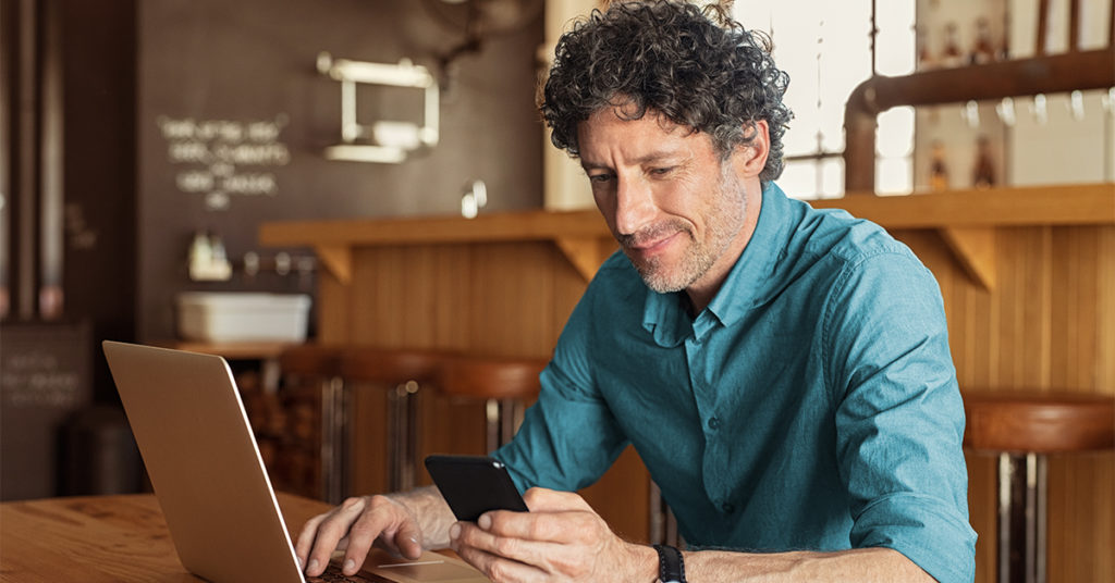 A man looking at his phone while working on a laptop