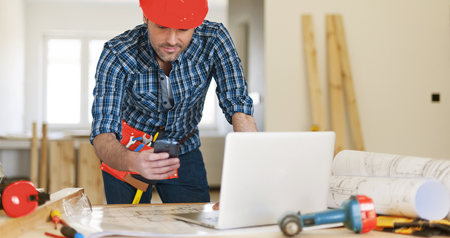 A contractor looking at his phone next to a desk with a computer